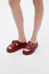 Sandalias planas de eco cuero color bordó, con tiras cruzadas y hebilla metálica dorada.