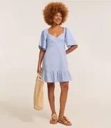 Vestido corto evasé color celeste, con escote en V, mangas cortas amplias, recorte cutout en los laterales de la cintura y volado en el bajo.