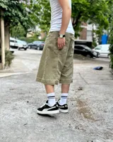 Bermuda de corte baggy color verde con efecto gastado. Presenta costura vertical trasera en cada pierna y detalle artesanal visible en el bajo. Incluye un cordón extra confeccionado en la misma tela.