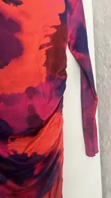 Vestido midi ajustado con estampado abstracto en tonos naranja, rosa y azul. Tiene cuello alto y mangas largas.