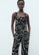 Pantalón de tiro medio confeccionado en mezcla de lino y viscosa, con diseño recto, bolsillos laterales, trabillas y cierre de botón y cremallera. Presenta un estampado de flores y hojas de estilo lineal en contraste.
