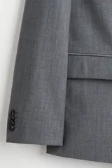 Blazer cruzado de color gris medio, con solapas de pico, ojal decorativo y cierre de doble botonadura. Presenta bolsillo superior insertado, bolsillos delanteros ribeteados con solapa y botones decorativos en los puños.