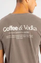Remera de algodón color marrón con efecto lavado, cuello redondo y estampa pequeña en el pecho con la frase Coffee & Vodka.