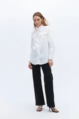 Camisa blanca de algodón con cuello alto con volados y bordado calado en el frente. Tiene mangas largas con puños abotonados y cierre frontal con botones.