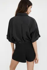 Camisa de corte fluido confeccionada en mezcla de modal, con cuello solapa, manga corta con dobladillo y bolsillo de plastrón en el delantero. Presenta cierre frontal con botones ocultos por tapeta y aberturas laterales en el bajo.
