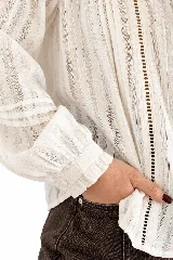 Blusa blanca de estilo romántico, confeccionada en tela liviana con detalles de alforzas y encaje insertion en el frente. Cuenta con cuello alto fruncido con lazo de ajuste, mangas largas abullonadas con puños elásticos y cierre frontal con botones.