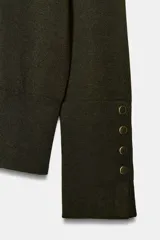 Jersey de punto liso con cuello redondo y manga larga. Presenta detalle de botones decorativos en los puños.
