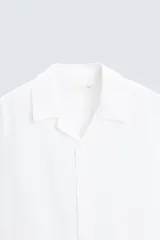 Camisa de lino color negro con calce relajado, cuello bowling y manga corta. Presenta cierre frontal con botones a tono y aberturas laterales en el bajo.