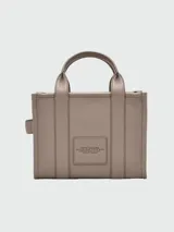 Cartera tipo tote de Marc Jacobs, confeccionada en cuero granulado color azul marino. Presenta el logo de la marca estampado en el frente, doble asa superior y correa ajustable y extraíble para llevar al hombro o cruzada.
