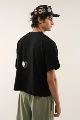 Remera negra de corte boxy y relajado, confeccionada en jersey de algodón con escote redondo acanalado. Cuenta con un estampado frontal en color blanco que combina un diseño de doble sol y la inscripción de la marca.