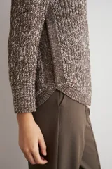 Sweater de punto con textura jaspeada en tonos marrones, de corte recto, cuello redondo y mangas largas. Presenta un diseño con ruedo curvo.