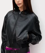 Campera bomber de cuero sintético negro, con cierre frontal de cremallera, cuello alto y puños y bajo elásticos con rib. Presenta costuras decorativas en los hombros.