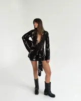 Vestido corto de mangas largas acampanadas, con escote profundo en V y detalle de lazo anudado en la cintura. Presenta un estampado abstracto tipo mármol en tonos blanco y negro.