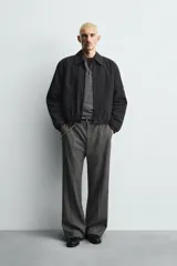 Cazadora de hombre de ajuste cropped fit, confeccionada en tejido de algodón con patrón de rayas verticales finas en tonos oscuros (negro/azul marino y marrón/beige). Presenta cuello solapa, cierre frontal de cremallera, bolsillos laterales y elástico en puños y bajo.