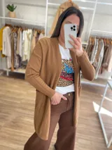 Saco largo color crema, de tejido de punto, con bolsillos laterales y corte recto.