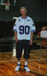 Camiseta estilo jersey de fútbol americano, color blanco, con cuello en V ribeteado en azul. Presenta el número "90" grande en el frente en azul marino con borde blanco. Tiene bordados en el pecho como "Lx." y "Ravers", y números pequeños en las mangas. Los puños tienen franjas azules y negras.