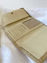 Billetera de cuero con diseño tricolor en tonos turquesa, blanco y beige, con textura tipo reptil. Cuenta con una solapa frontal con cierre de broche y una etiqueta de cuero con el logo grabado.