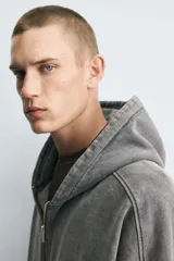 Sudadera con capucha y cierre de cremallera, de corte relajado (relaxed fit), confeccionada en algodón con interior afelpado. Presenta bolsillos frontales tipo canguro y acabados en rib. El tejido tiene un efecto lavado que le da un color negro desgastado.