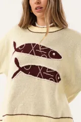 Sweater color manteca de tejido de punto con cuello redondo y ribete marrón. Presenta dos peces marrones tejidos en el frente con detalles bordados a mano.