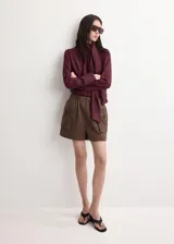 Blusa de manga larga bordó con cuello alto y detalle de fular integrado para anudar al cuello, corte recto y puños abotonados.