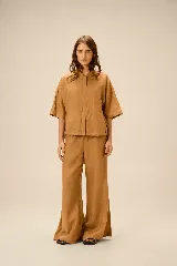 Chaqueta de lino y rayón color tostado, de corte holgado, mangas cortas amplias, cuello mao y cierre frontal oculto con cremallera. Presenta pespuntes a contratono en las costuras y cordón ajustable en el bajo.
