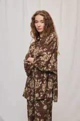 Camisa de silueta amplia y largo por debajo de la cadera, confeccionada en tela liviana con estampado floral en tonos marrón y tostado. Presenta cuello clásico, cierre frontal con botones y mangas tres cuartos.