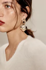 Pendientes colgantes de metal dorado con diseño orgánico y aplicación de piedra central transparente.