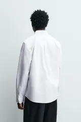 Camisa de corte regular fit confeccionada en tejido de algodón con diseño de rayas verticales. Presenta cuello abotonado, manga larga con puños abotonados, bolsillo plastrón en el pecho y cierre frontal con botones.