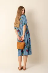 Vestido largo estampado con flores en tonos violeta, naranja, verde y azul sobre un fondo beige claro. Tiene cuello en V y mangas cortas.