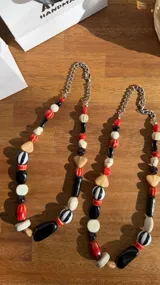 Collar de diseño artesanal confeccionado con cuentas de diferentes formas, tamaños y materiales en tonos rojo, negro, blanco y beige, acompañado por una cadena de eslabones plateados.