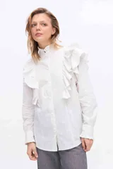 Camisa blanca de manga larga con volados en el delantero y los hombros, cuello alto con terminación de volados y cierre frontal de botones.