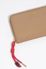 Billetera Bimba y Lola de cuero sintético color beige, con cierre perimetral y logo grabado en letras doradas. Incluye un tirador de cierre con cordón rojo y detalles de cuentas.