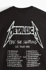 Remera negra de corte holgado con hombros caídos y cuello redondo. Presenta un estampado frontal pequeño con el logo de Metallica y la inscripción 'U.S. Tour 1985'.