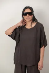 Blusa de lino color marrón oscuro, con escote redondo, mangas cortas amplias y detalle de alforzas verticales en el lateral derecho.