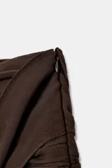 Falda pantalón de tiro bajo en color negro, con cintura drapeada y detalle de tira lateral colgante. Presenta un diseño con volantes en el bajo y cierre de cremallera metálica.