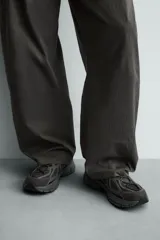 Zapatilla deportiva de estilo running, completamente negra, con capellada de malla y superposiciones sintéticas. Presenta una suela gruesa y voluminosa con diseño segmentado.