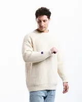 Sweater de punto de lana merino color off-white, con cuello redondo y diseño relajado. Presenta un pequeño detalle bordado a mano en la manga.