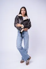 Campera tipo gamulán de cuero sintético marrón oscuro con interior y detalles de corderito sintético en cuello y puños. Presenta cierre frontal, bolsillos laterales con cierre y correas ajustables en el cuello.