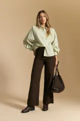 Camisa blanca de manga larga con cuello y botones frontales. Presenta detalles de volados o puntilla en los hombros y mangas abullonadas con puños anchos. La tela parece tener un sutil tejido a rayas verticales.