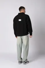 Buzo de cuello alto con cierre frontal parcial, manga larga y diseño holgado. Presenta un pequeño logo bordado en el pecho.