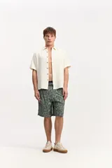 Short de baño estilo surf color gris, de largo medio, con estampado geométrico abstracto y cordón ajustable en la cintura. Incluye bolsillo trasero con solapa.