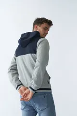 Campera de felpa gris con capucha y cordón ajustable, cierre frontal con cremallera, bolsillos laterales, mangas largas y logo estampado en el pecho.