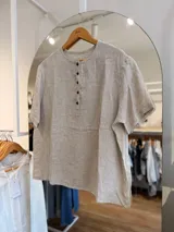 Blusa de lino color beige con cuello redondo, mangas cortas y cierre frontal parcial con botones oscuros.