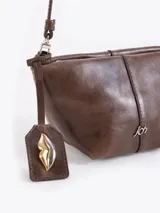 Bandolera de cuero vacuno con silueta estructurada, cierre superior y aplique metálico frontal. Incluye correa regulable y tag colgante con detalle decorativo.