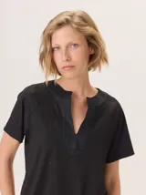 Remera negra de manga corta con escote en V y cuello redondo abierto. El cuerpo de la prenda tiene un acabado brillante o con lurex, mientras que el cuello es de un material liso y opaco.