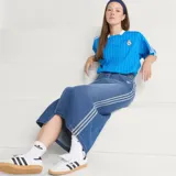 Camiseta de fútbol Adidas del Real Madrid, inspirada en los años 80. Diseño de color azul con finas rayas verticales blancas, cuello en V blanco, mangas cortas con las tres tiras características de la marca y escudo retro del club bordado en el pecho.