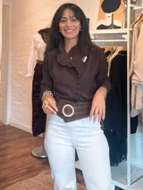 Camisa de color marrón oscuro con cuello mao y detalle de volados a lo largo de la abertura frontal. Presenta mangas largas con puños rectos y cierre frontal mediante botones ocultos.