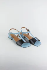 Sandalias planas de cuero con taco cuadrado bajo de 2 cm, diseño bicolor en celeste y negro, con tira en T y pulsera ajustable al tobillo con hebilla metálica.