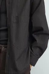 Sobrecamisa de corte relajado confeccionada en denim de algodón con diseño a rayas verticales. Presenta cuello solapa, cierre frontal de botones, manga larga con puños abotonados y un bolsillo plastrón en el pecho.