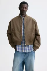 Campera bomber de nylon levemente acolchada, con cuello, puños y bajo acanalados. Presenta cierre frontal, bolsillos laterales con botón a presión y un bolsillo con cierre en la manga.